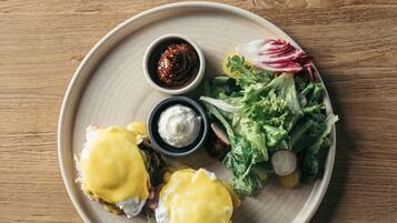 A plate with food items including eggs benedict, a salad, and condiments on a wooden table.