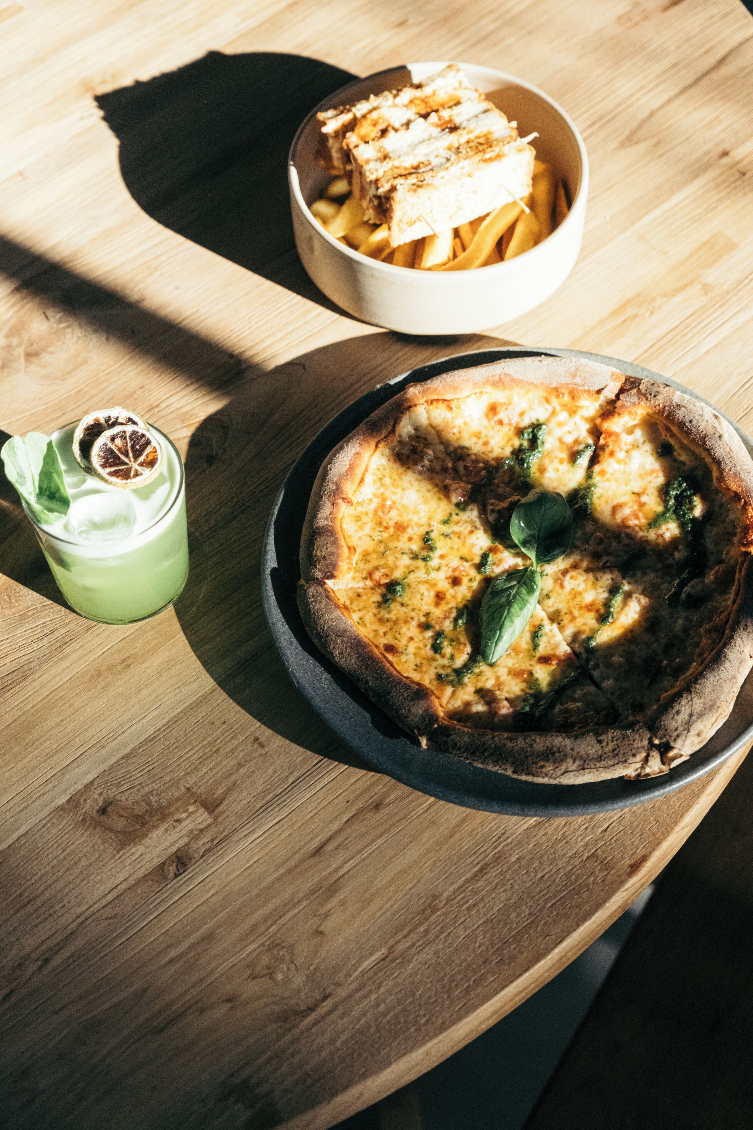 A pizza and a bowl of fries on a wooden table.
