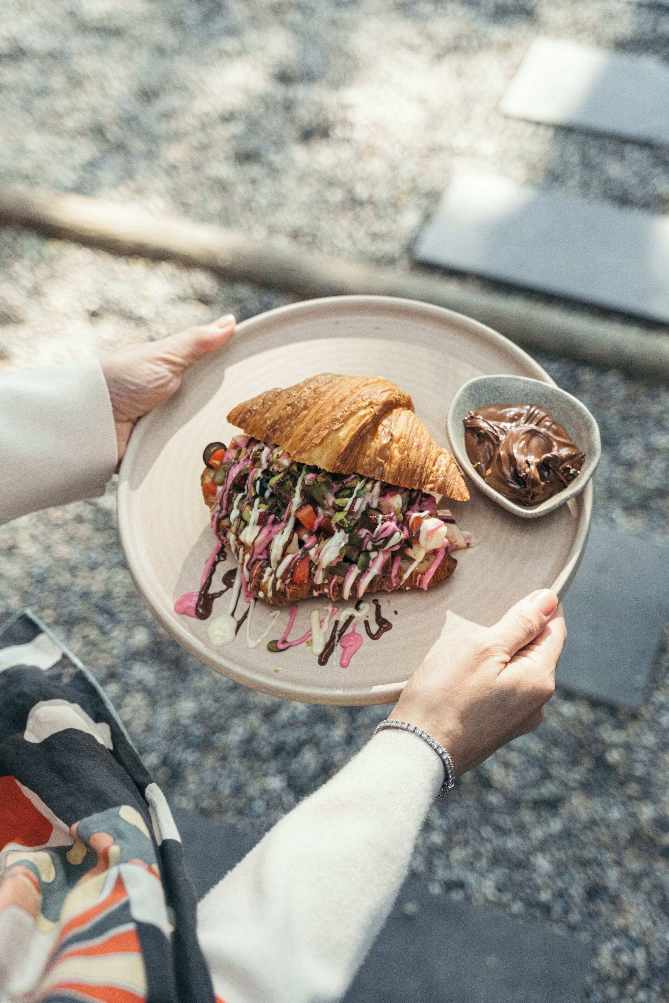 A person holding a plate with a sandwich and a small bowl of chocolate sauce.