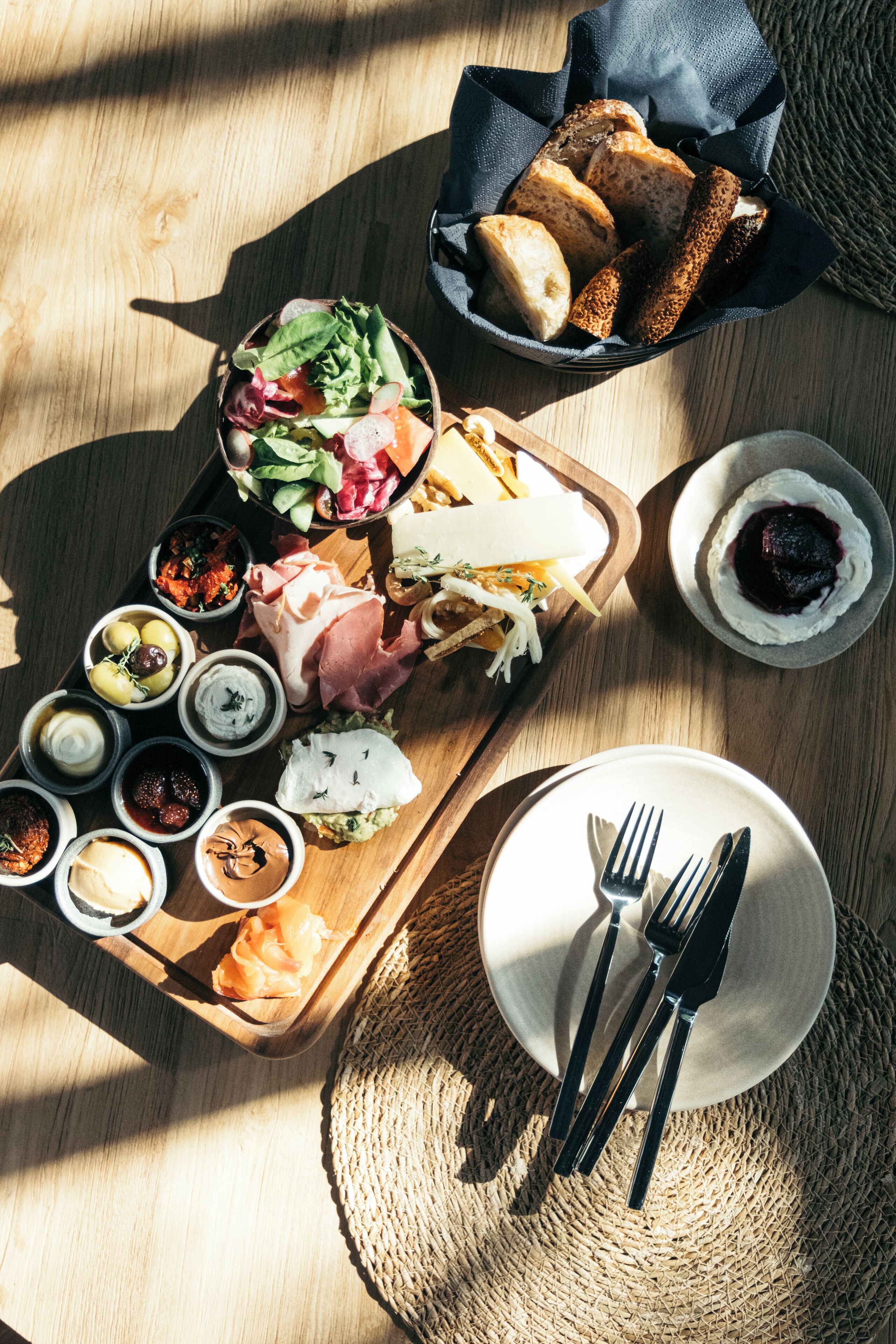 A wooden serving tray with various cheeses, meats, and dips on a table.