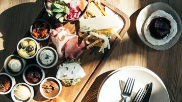 A wooden serving tray with various cheeses, meats, and dips on a table.