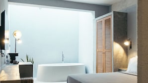 A modern bedroom with a large bed, a ceiling fan, a bathtub, and a view of the sky.