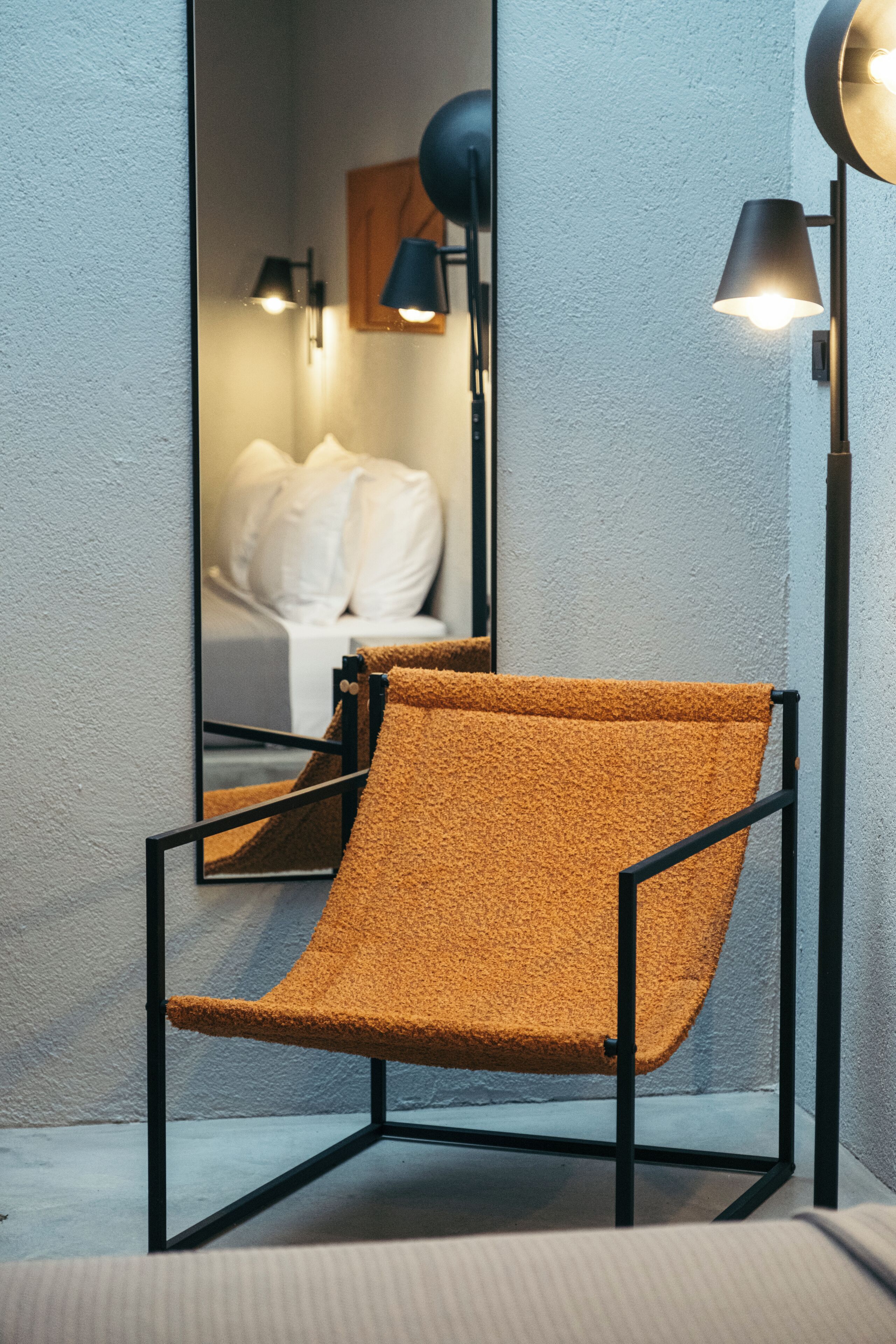 A modern room with a mirrored wall, a black metal chair, and two floor lamps.