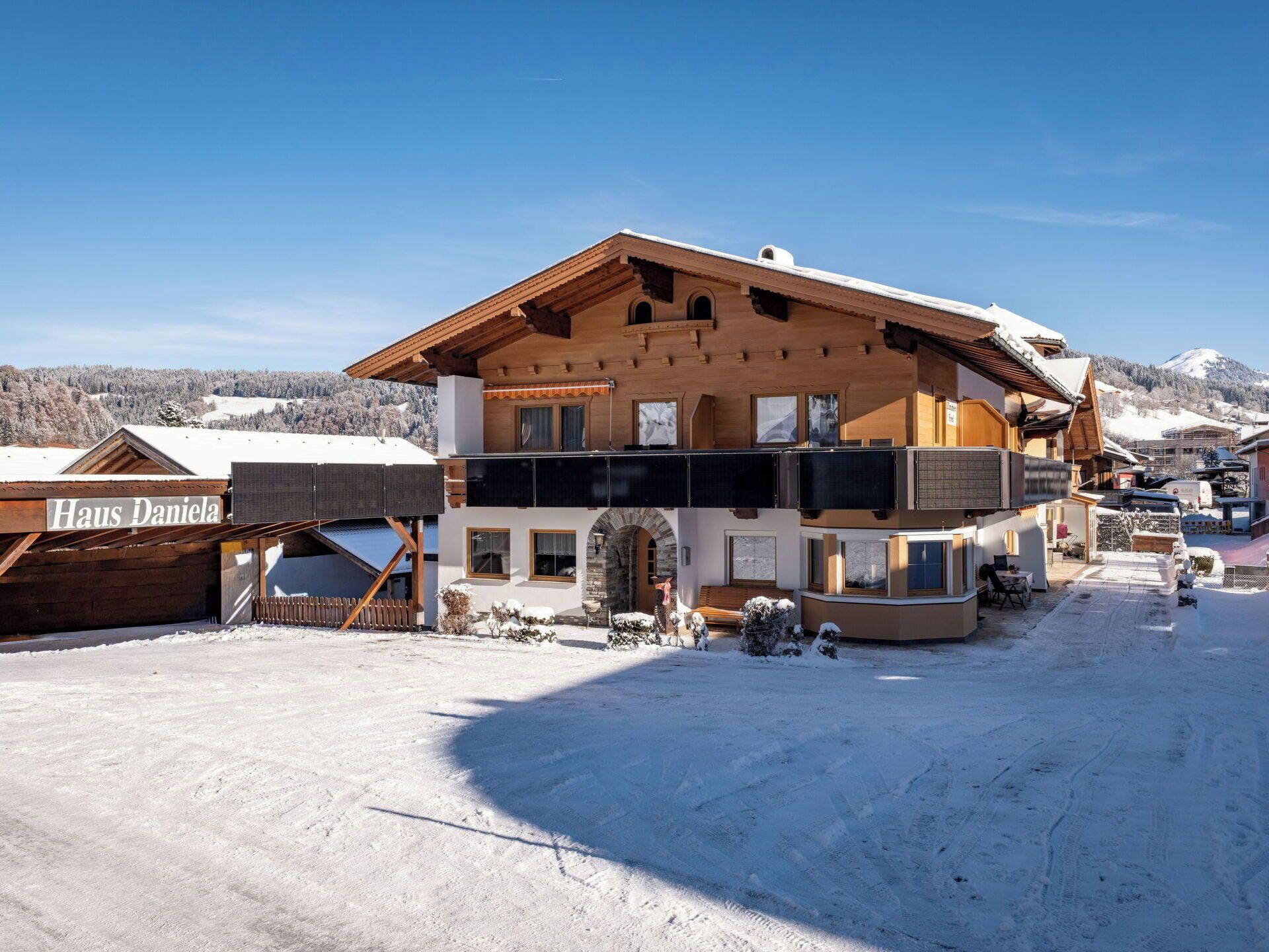 A two-story chalet with a wooden facade, a balcony, and a ski lift nearby.