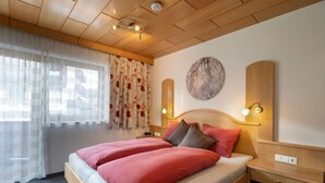 Ein Hotelzimmer mit einem hölzernen Bett, einem Nachttisch, einer Wandlampe und einem Fenster mit transparenten Vorhängen.