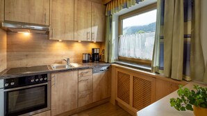 Eine moderne Küche mit Holzschränken, Edelstahlgeräten, einem Fenster mit Vorhängen und einer Pflanze auf der Arbeitsplatte.