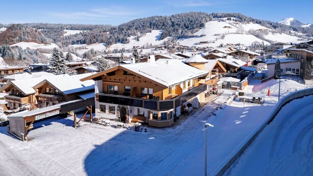 Ein schneebedecktes Dorf mit Holzbauten, darunter ein auffälliges Haus namens "Haus Daniela".