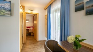 Ein Hotelzimmer mit Holzboden, einem Esstisch mit Blumenvase, einer Couch und Blick auf eine gebirgige Landschaft durch das Fenster.