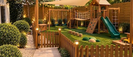 A wooden play structure with a slide and climbing wall in a backyard.