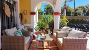 Une terrasse ensoleillée, meublée de meubles en osier, avec une table sur laquelle repose un panier tressé, et des plantes en pot.