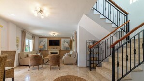 Un salon spacieux doté d’une cheminée, de sièges confortables et d’un escalier avec une rampe en bois.