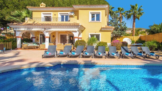 Un espace piscine avec des chaises longues et un bâtiment jaune doté d’un toit en tuiles.