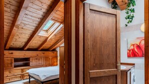 A wooden room with a sloped ceiling, a bed, a wooden wardrobe, and a bathroom with a washing machine.