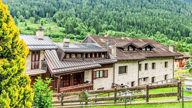 A traditional chalet with a sloped roof, wooden balconies, and a view of a forested valley.