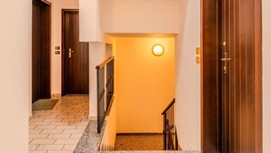 A hallway with a wooden door on the right, a light fixture on the wall, and a tiled floor.
