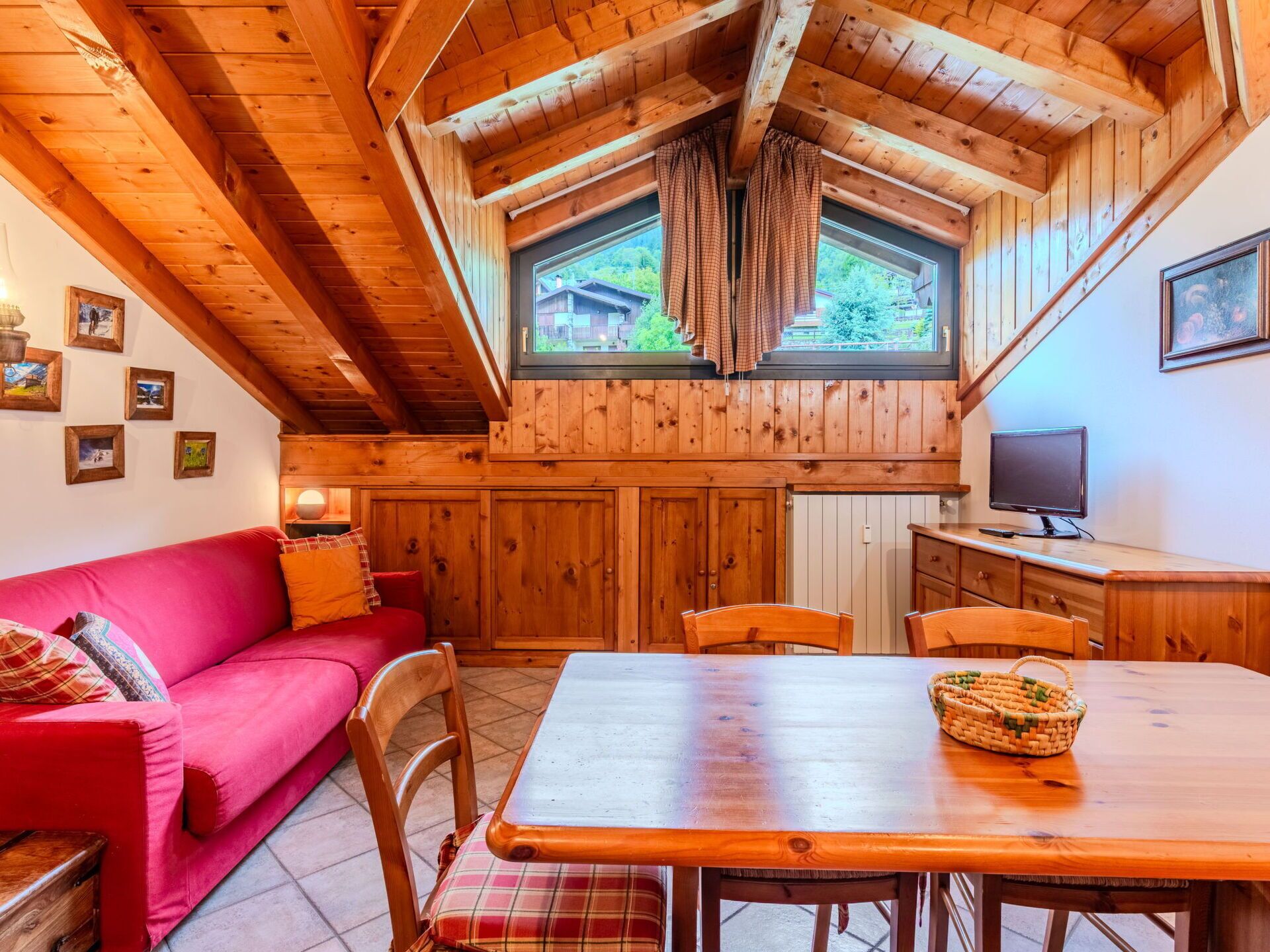 Een gezellig interieur van een chalet met een houten plafond, een rode bank, een eettafel en een televisie.