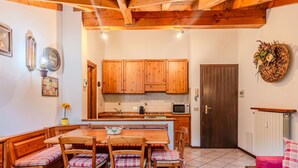 A cozy kitchen with wooden cabinets, a dining table with plaid chairs, and a red sofa.