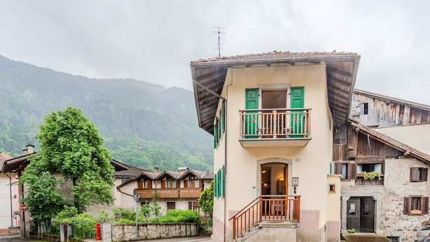 Un bâtiment traditionnel doté d’un balcon, situé dans une rue pavée, avec une chaîne de montagnes en arrière-plan.