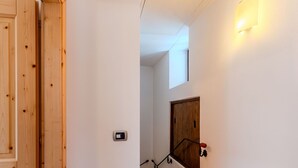 Une porte en bois, un luminaire fixé au mur, un escalier avec une rampe et une porte en bois en haut de l’escalier.