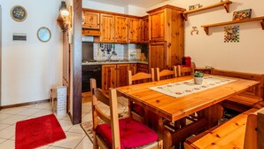 A wooden dining table with chairs, a kitchen with wooden cabinets, and a red rug on the floor. - Beautiful apartment for 6 guests with WIFI, TV and balcony (Spiazzo)