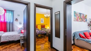 A modern apartment with a wooden herringbone floor, a bed with patterned bedding, a sofa with red cushions, and a colorful abstract painting on the wall. - Beautiful apartment for 5 guests with A/C, WIFI and patio (Greve In Chianti)