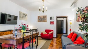A living room with a dining area, a red sofa, a TV, and artwork on the walls. - Beautiful apartment for 5 guests with A/C, WIFI and patio (Greve In Chianti)