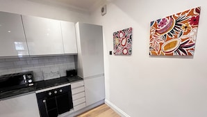Una cucina moderna con mobili bianchi, un piano di lavoro nero e un tostapane. Due quadri colorati adornano la parete.