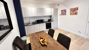 Una cucina moderna con mobili bianchi, un piano di lavoro nero e un'area pranzo con tavolo e sedie in legno.
