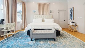 Une chambre à coucher avec un grand lit, une table de chevet, une chaise, un bureau et une fenêtre avec des rideaux.
