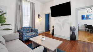A modern living room with a sofa, a patterned armchair, a coffee table, and a flat-screen TV mounted on the wall.