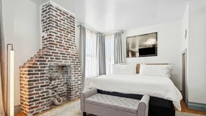 A bedroom with a brick fireplace, a large bed, a bench, and a flat-screen TV.