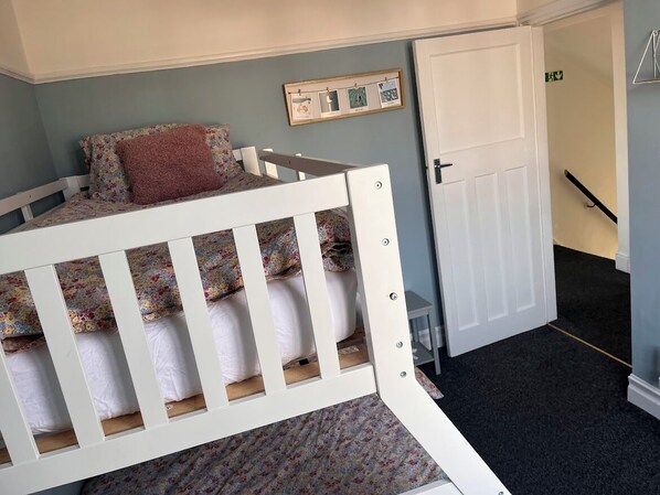 A bedroom with a white bunk bed, a door, and a small table.