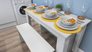 Ein ordentlich gedeckter Esstisch mit weißen Tellern, gelben Platzsets und Schüsseln voller Snacks.