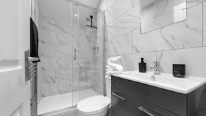 Ein modernes Badezimmer mit einer Duschkabine, einer weißen Toilette und einem Waschtisch mit Spiegel.