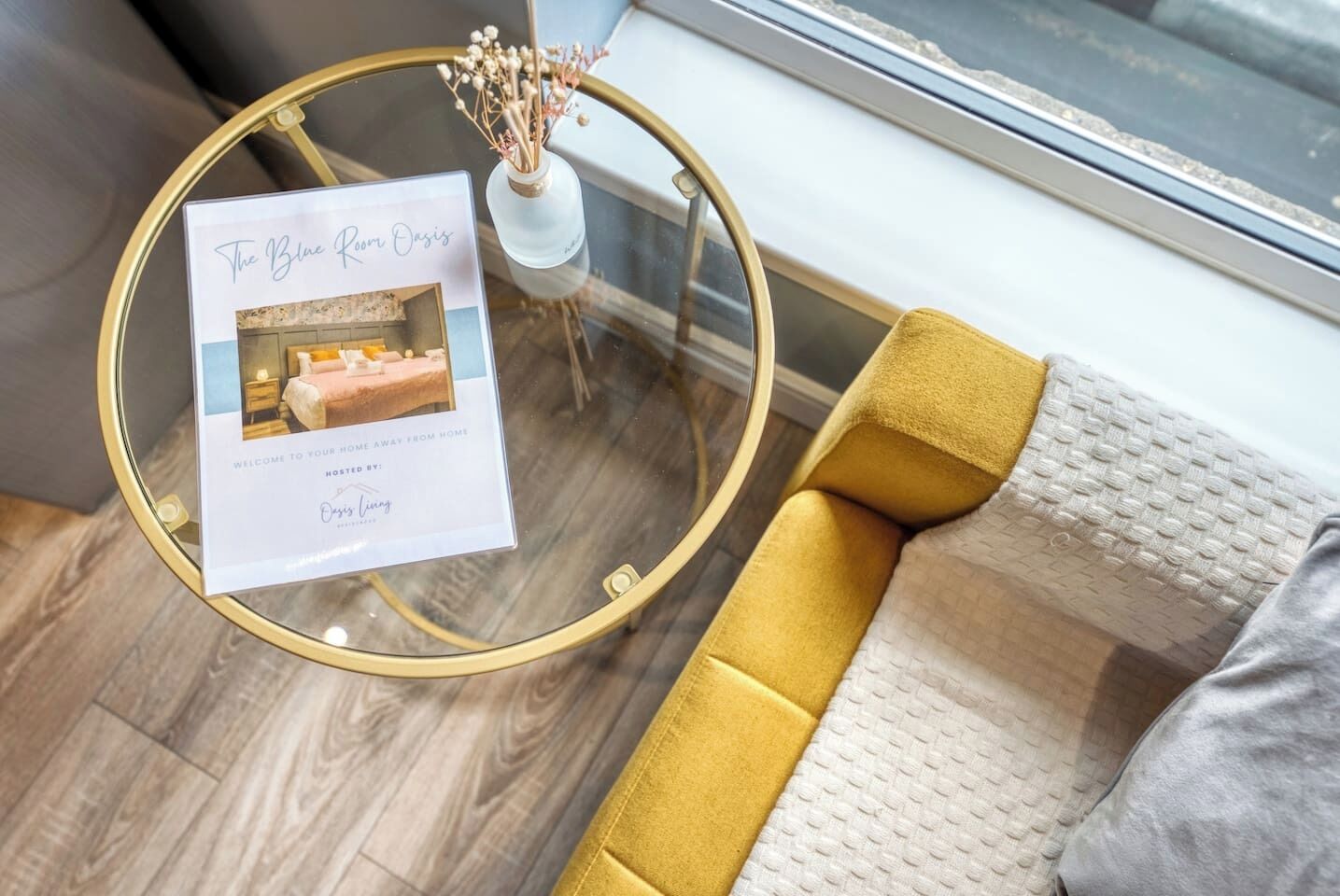 A glass table with a framed brochure titled "The Blue Room Oasis" and a vase with dried flowers.
