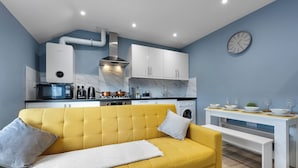 Eine kompakte Küche mit modernen Geräten, ein gelbes Sofa und ein Essbereich mit einem weißen Tisch.