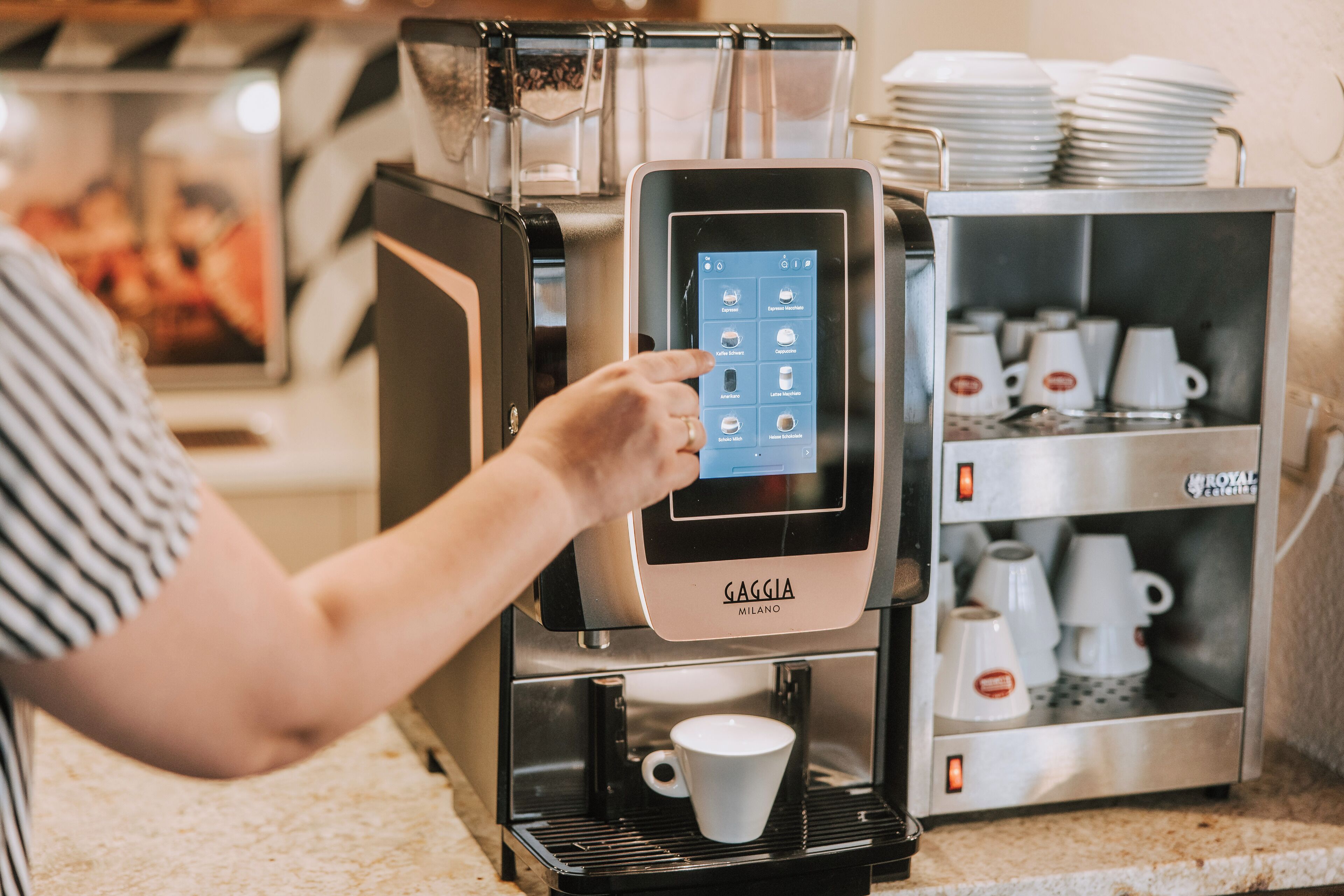 A coffee machine with a touchscreen interface, a cup dispenser, and a coffee pot.