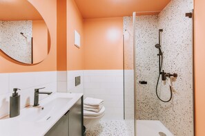A modern bathroom with a glass-enclosed shower, white sink, and a round mirror. - Velotique Hotel Angelika - Self-Check-in (Hard)
