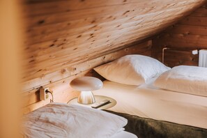A cozy wooden cabin bedroom with a single bed, a bedside table with a lamp, and a power outlet.