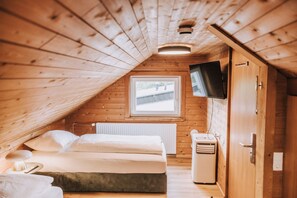 A cozy attic bedroom with a bed, a heater, a TV, and a window. - Velotique Hotel Angelika - Self-Check-in (Hard)