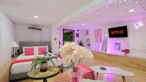 A modern hotel room with a bed, bedside table, and a TV displaying 'NETFLIX'. - Barbiecore Dream Pad in Sacramento! (Sacramento)