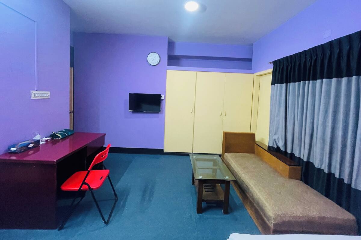 A small room with a desk, two chairs, a sofa, a TV, and a wardrobe.