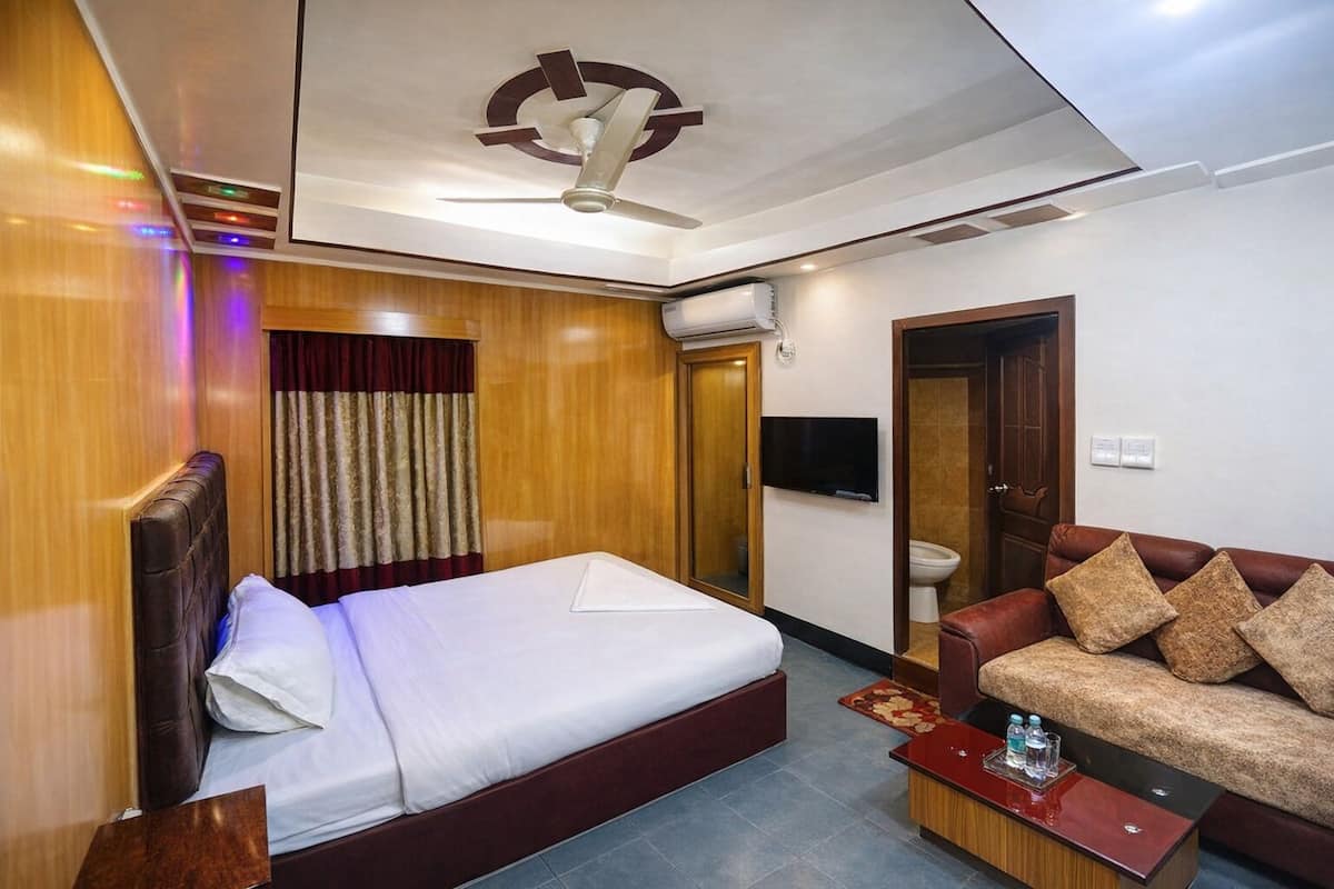 A hotel room with a bed, a sofa, a television, and an air conditioning unit.