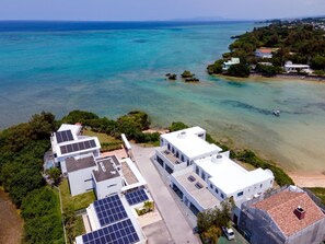 Ein Luftbild eines Küstengrundstücks mit modernen Gebäuden, Solaranlagen und freiem Blick auf das türkisblaue Meer.