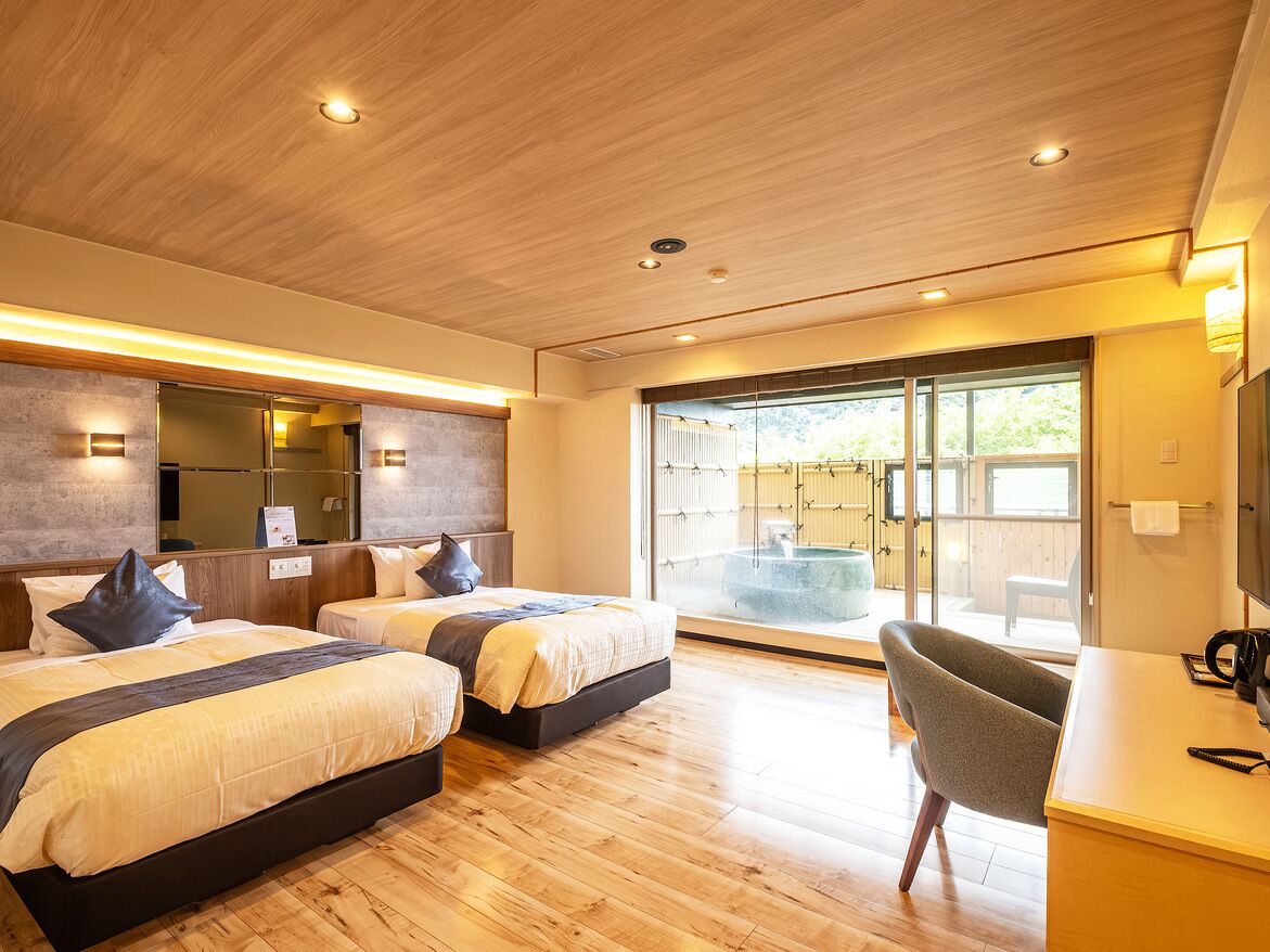 Habitación de hotel moderna con dos camas, un escritorio y vistas a un jacuzzi a través de una puerta de vidrio.