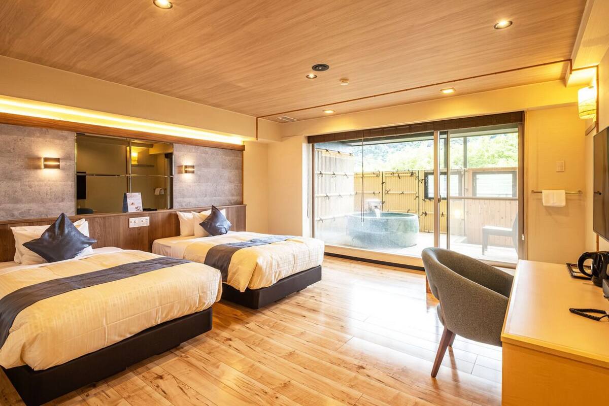 Habitación de hotel moderna con dos camas, un escritorio y vistas a un jacuzzi a través de una puerta de vidrio.