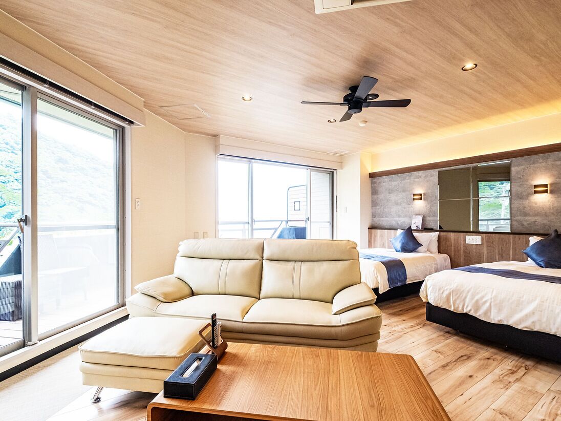 Un dormitorio moderno con sofá, cama, ventilador de techo y ventanas amplias.