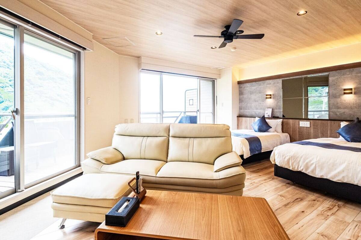 Un dormitorio moderno con sofá, cama, ventilador de techo y ventanas amplias.