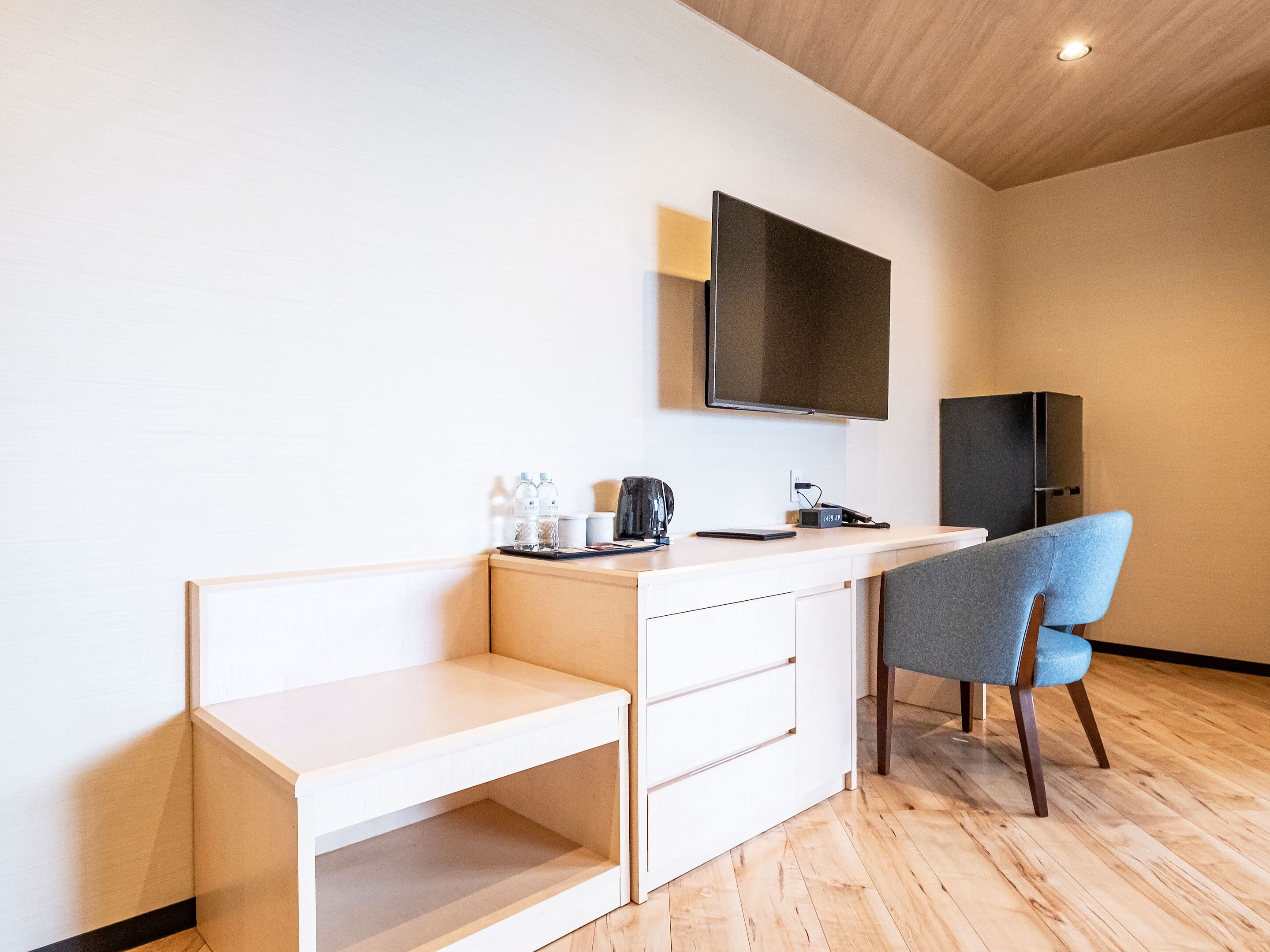 Quarto moderno e minimalista com escrivaninha de madeira, uma cadeira, televisão de tela plana na parede e um pequeno armário.