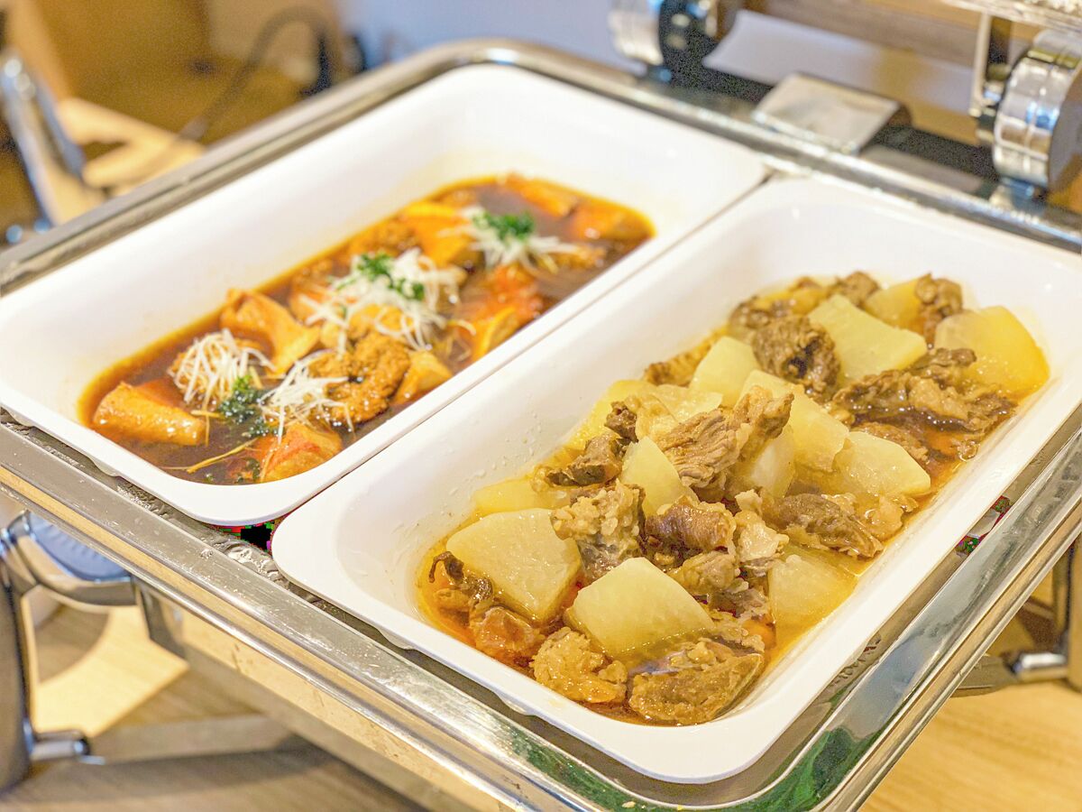 Two dishes of food, one with meat and potatoes and the other with a red sauce and vegetables, served on a tray.